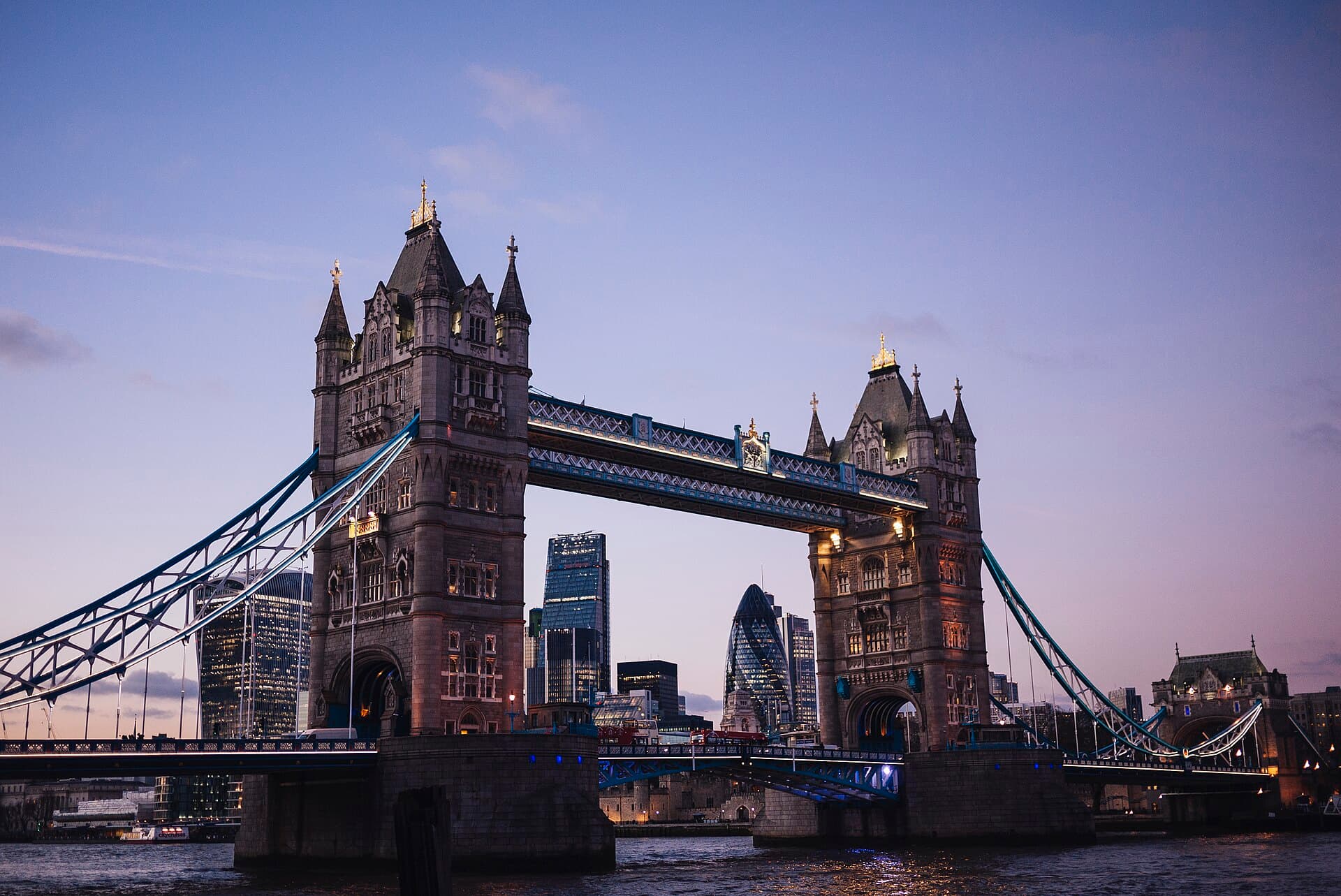 Tower Bridge de Londres iluminado al atardecer sobre el río Támesis, con los rascacielos de la City al fondo