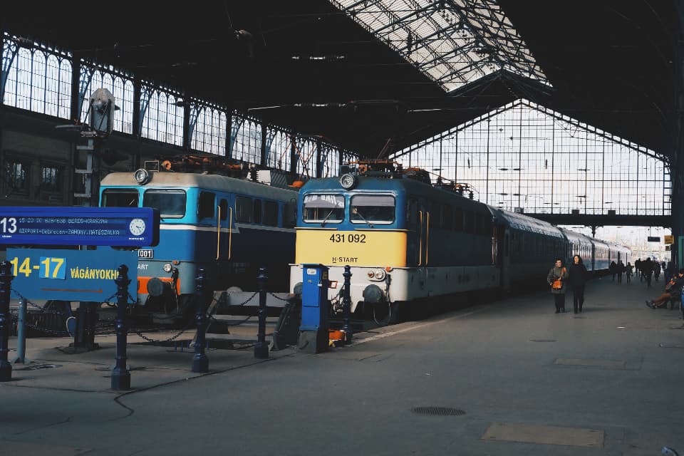 Trenes esperando bajo la marquesina de hierro y cristal de una estación ferroviaria europea, con viajeros en el andén